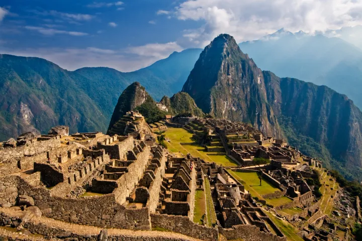 Photograph of Machu Picchu’s stone buildings beneath Huayna Picchu in morning light.